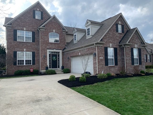 Brick house with black shutters, white garage door, and landscaped yard with green grass and black mulch.