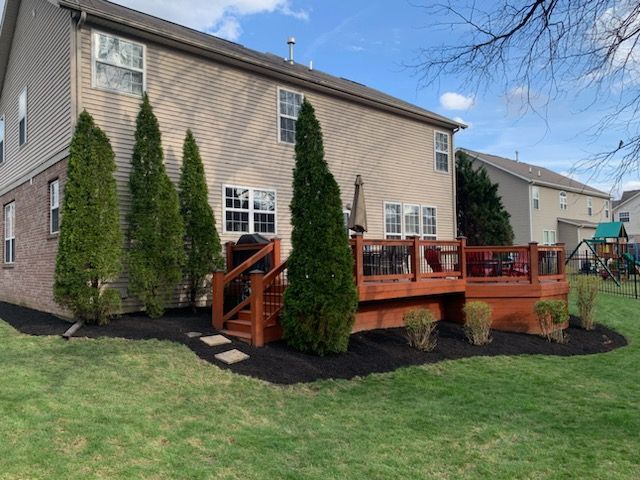Backyard view of a two-story house with a stained wooden deck, green lawn, and trees.
