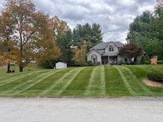 A house with a well-maintained lawn, striped with mowing patterns, under a cloudy sky.