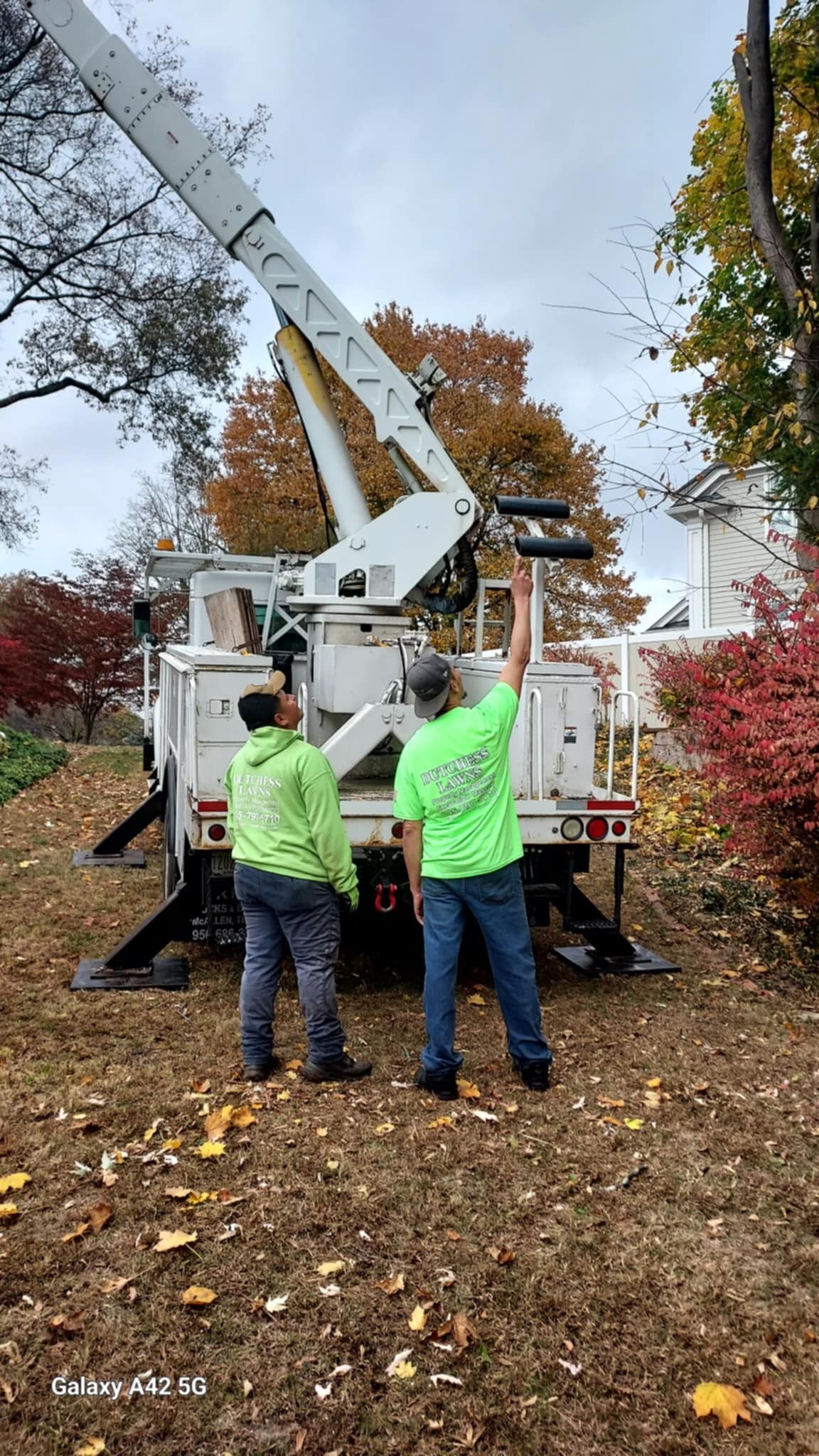 Two men in green shirts are standing in front of a crane.