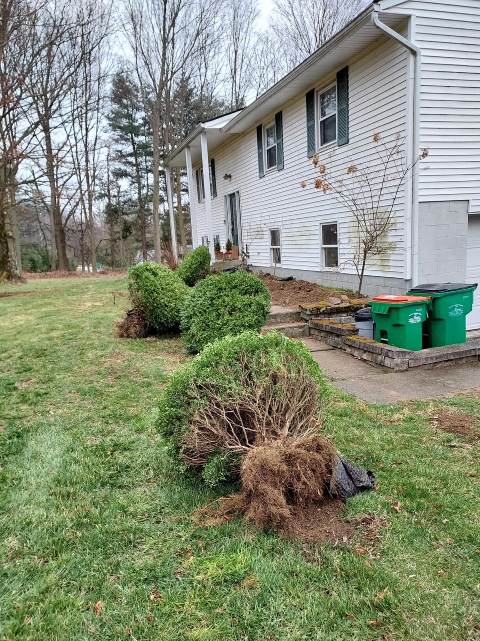 A white house with green trash cans in front of it.