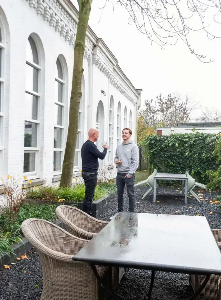 Voor een wit gebouw staan ​​twee mannen met elkaar te praten.