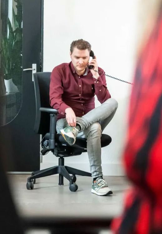 een man zit in een bureaustoel en praat aan een telefoon.
