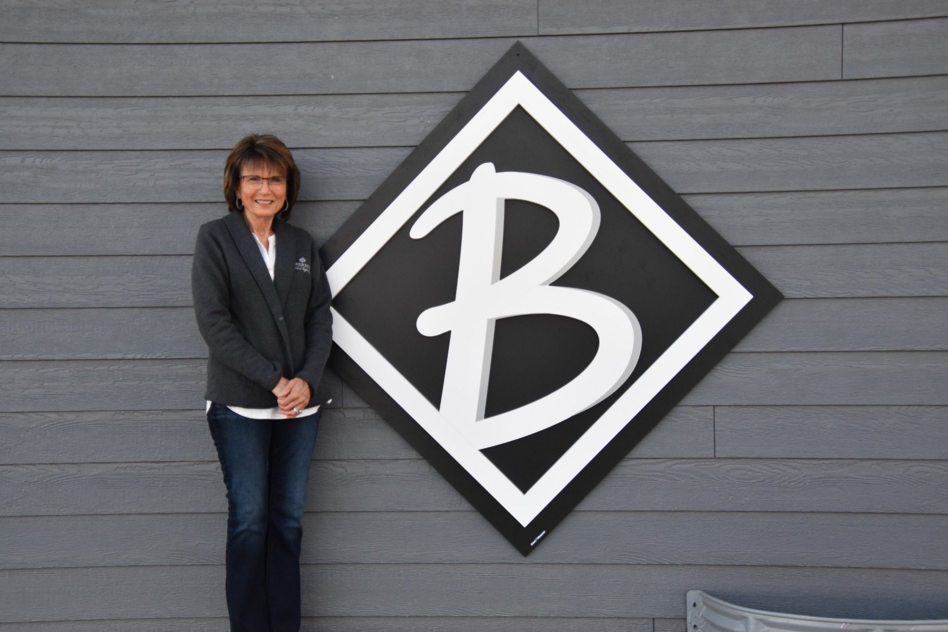 Woman standing beside a large, diamond-shaped logo with a stylized white