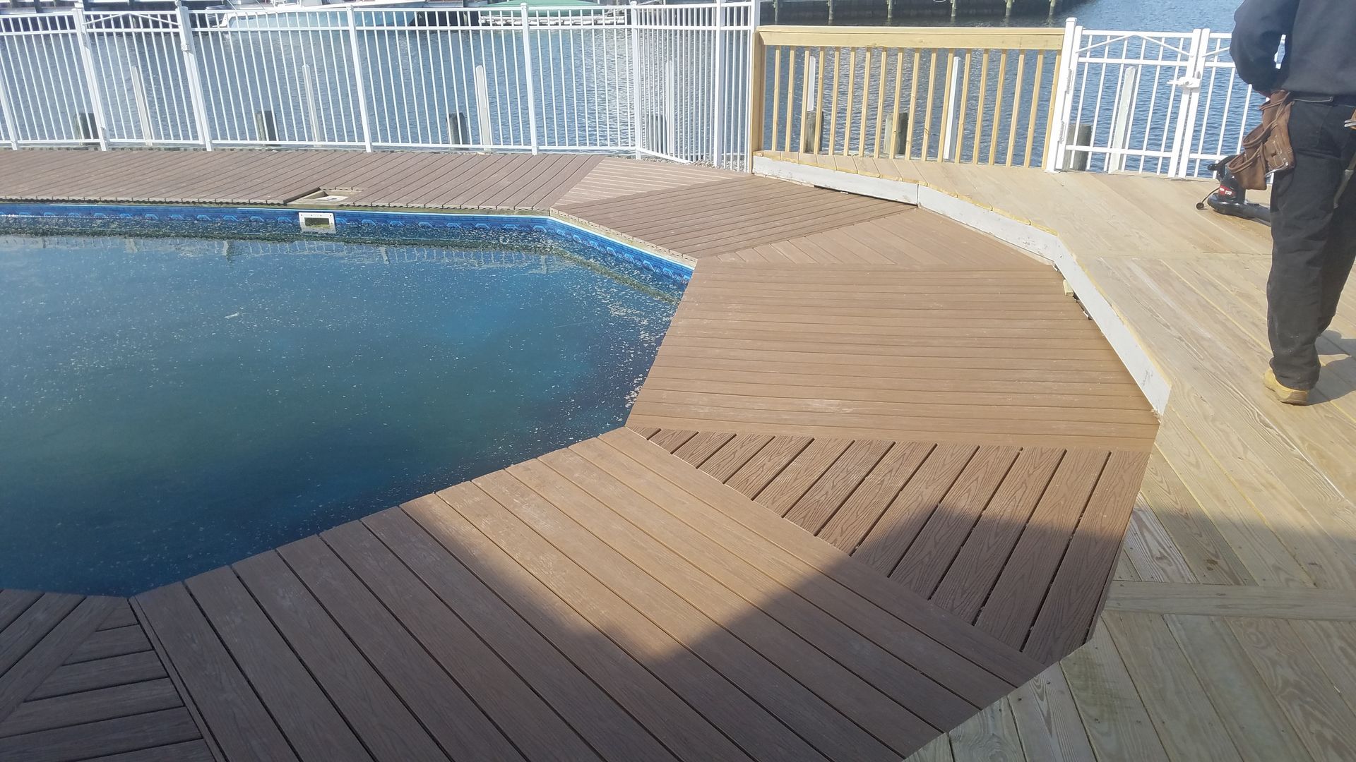 A man is standing next to a swimming pool with a wooden deck.