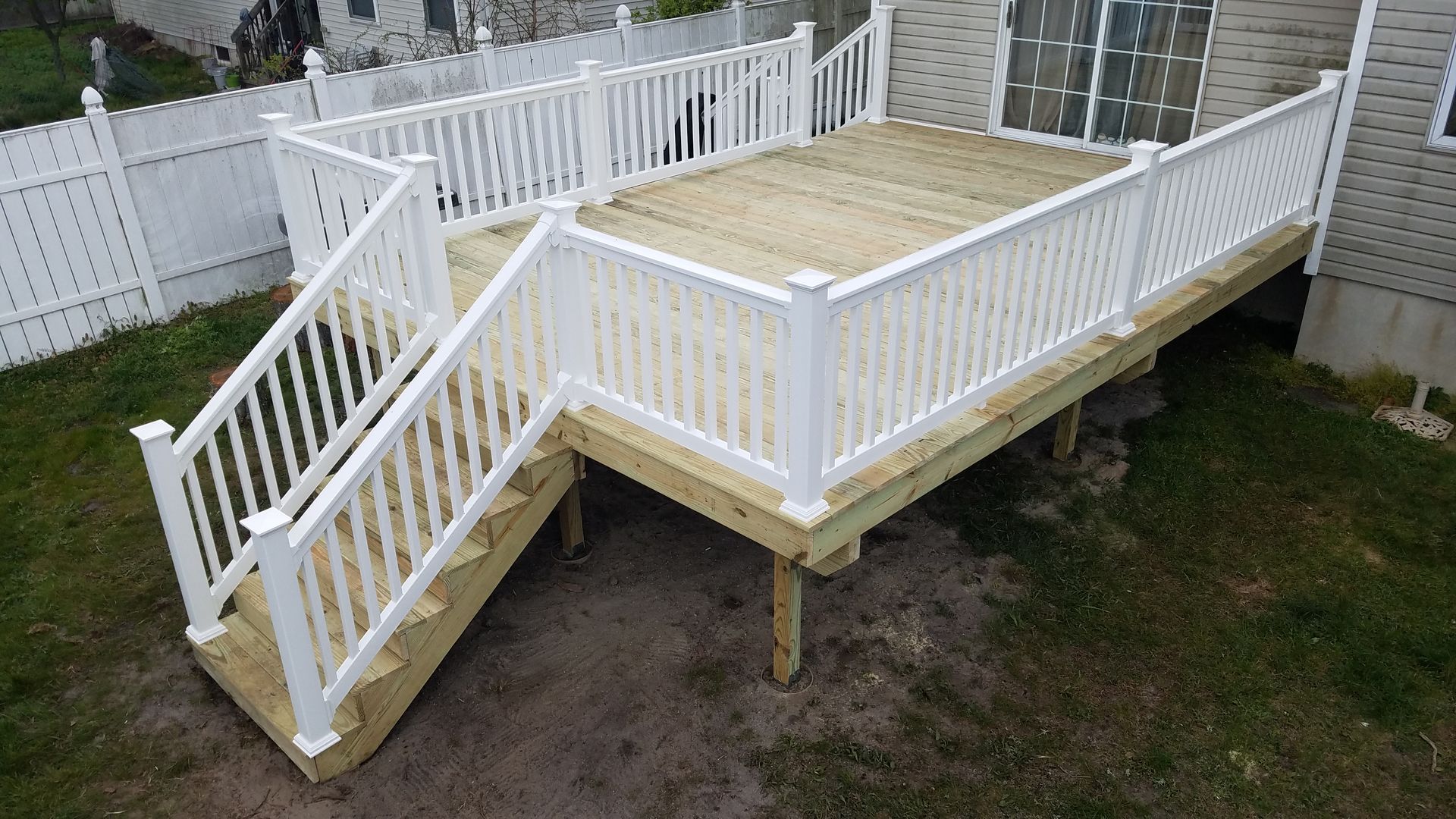 A wooden deck with white railings and stairs in a backyard.