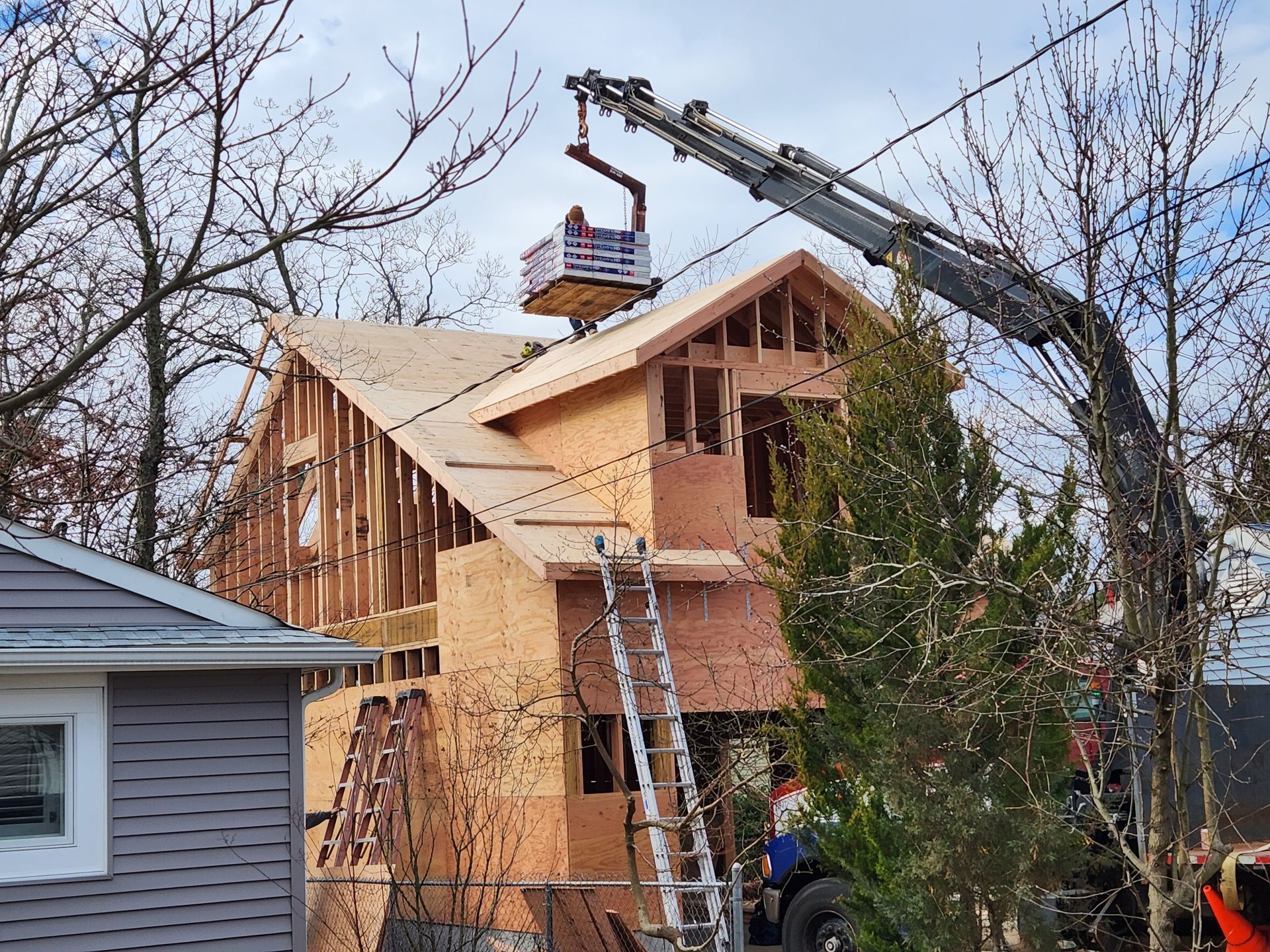 A crane is lifting a piece of wood on top of a house under construction.
