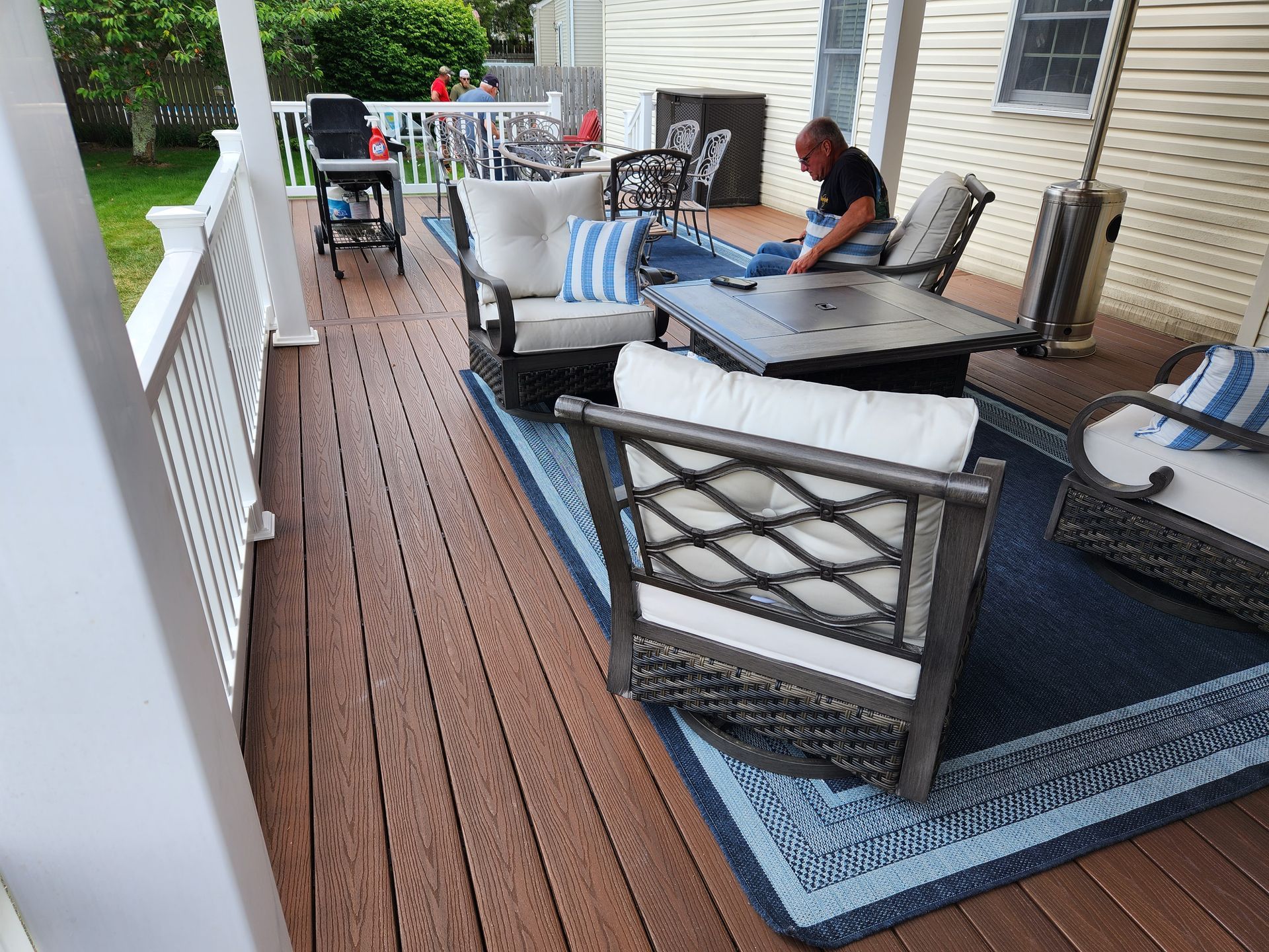 A man is sitting on a wooden deck with chairs and a table.