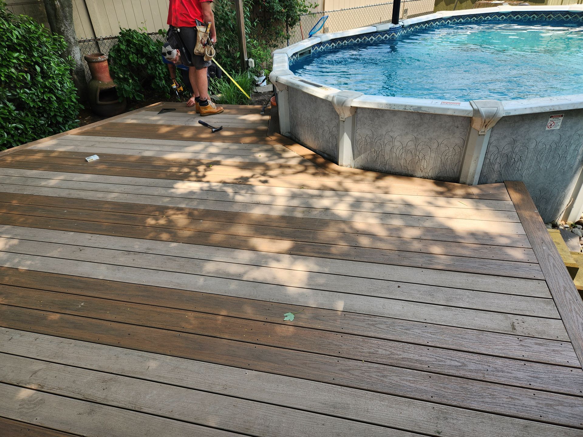 A man is standing on a wooden deck next to a swimming pool.