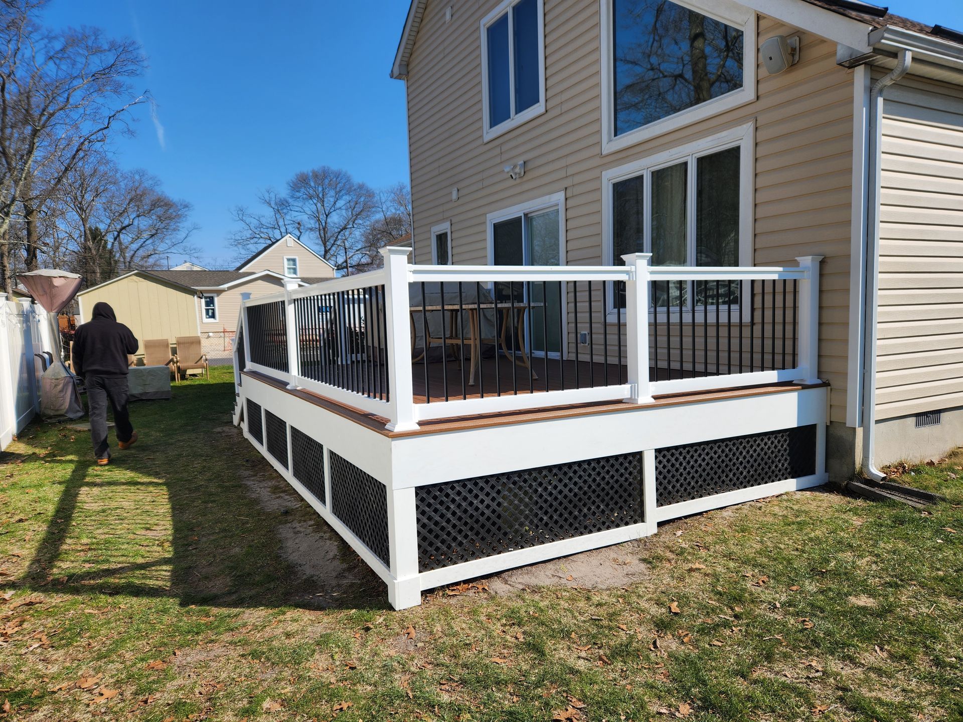 A large deck with a white railing is in the backyard of a house.