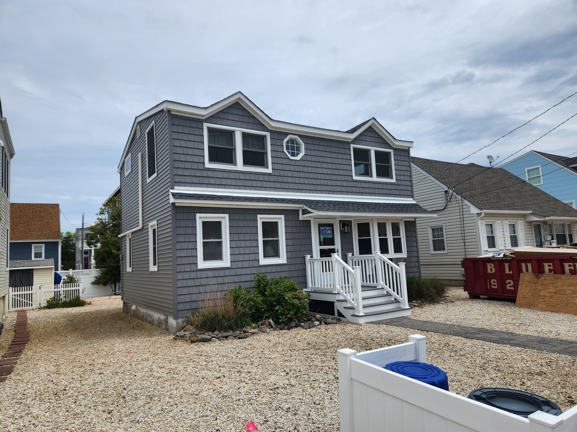 A gray house with white trim and a white fence in front of it.