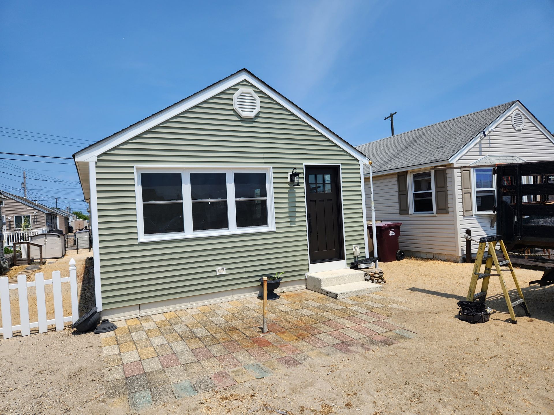 A small house with a green siding and a white fence in front of it.