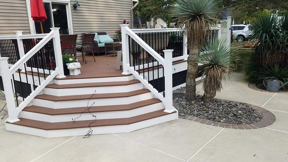 A deck with stairs leading up to it and a house in the background.