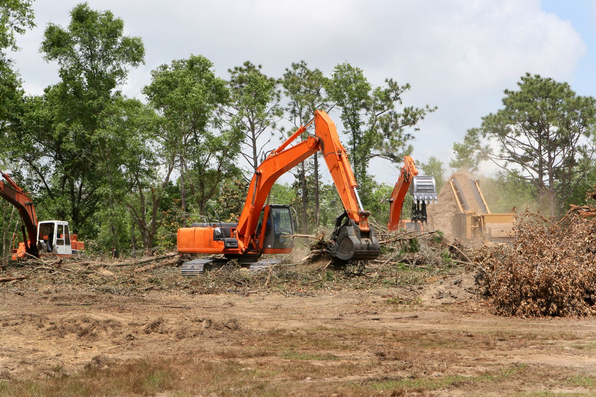 two excavators are working in a field with trees in the background .