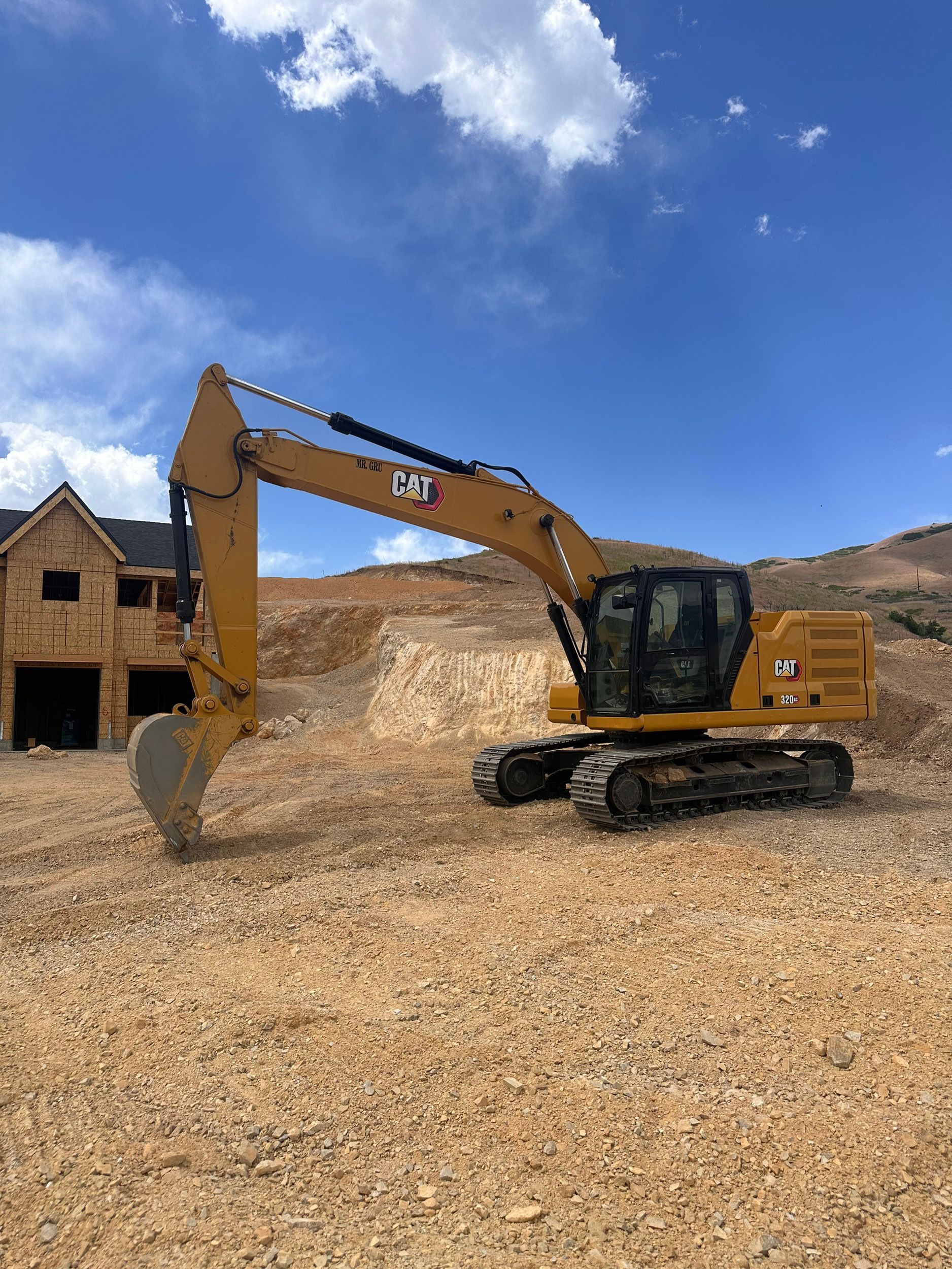 A yellow Caterpillar excavator on a construction site with a partly built house and a blue sky in the background.