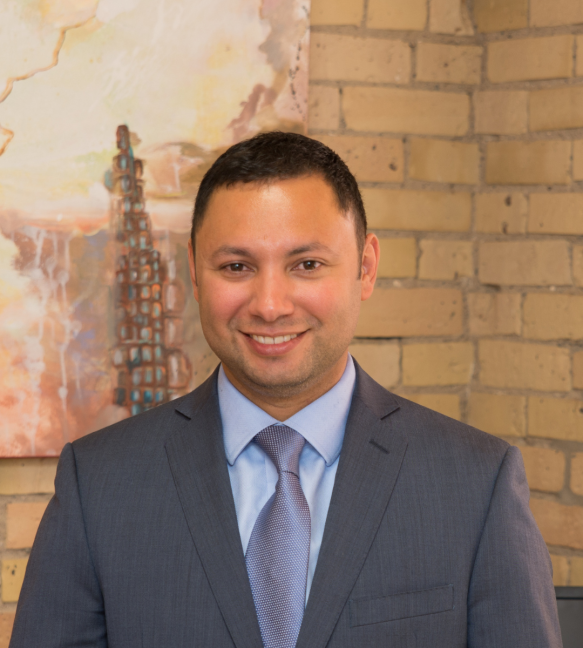 Man in suit smiles in front of a brick wall and abstract painting.