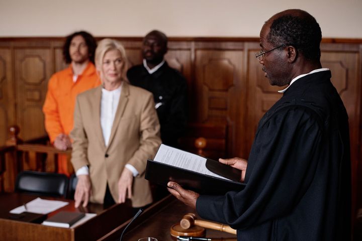 Judge reads documents in courtroom; lawyer and prisoner stand by.