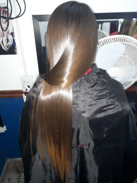 Cabello largo, liso y castaño con un brillo lustroso, visto desde atrás en una silla de peluquería.