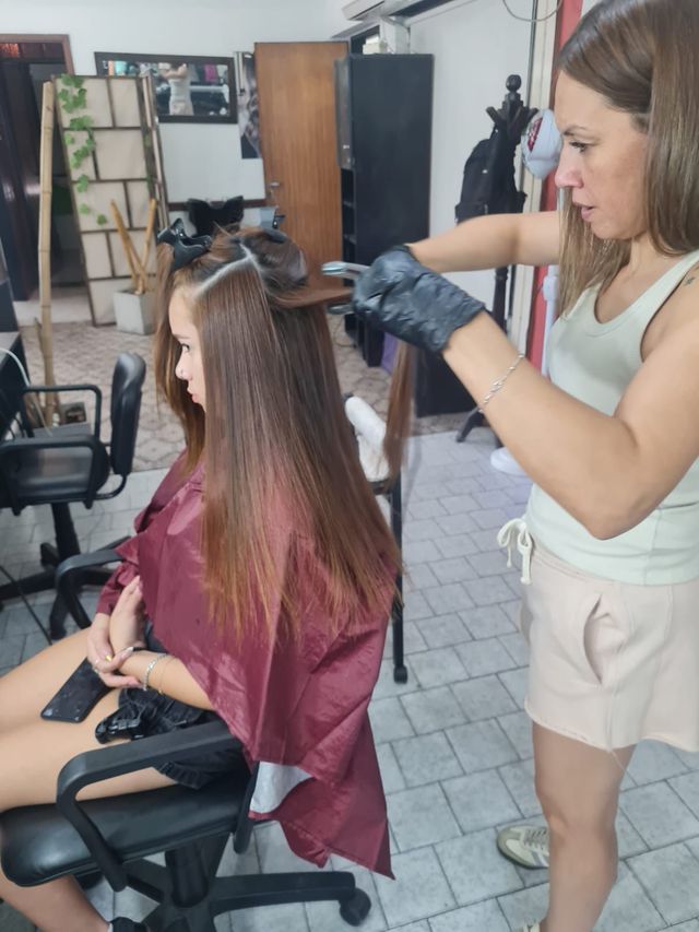 Peluquera aplicando un tratamiento a una clienta sentada en un salón luminoso.
