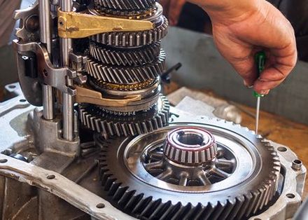 A person is working on a gearbox with a screwdriver.