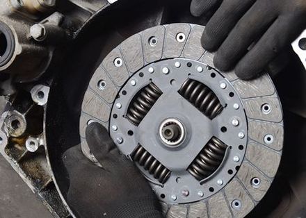 A person is holding a clutch plate on top of a car engine.