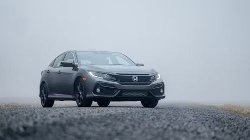 Gray Honda Civic driving on a wet road in a foggy, overcast setting.
