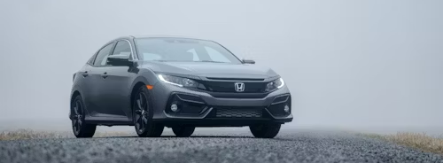 Gray Honda Civic driving on a wet road in foggy conditions.