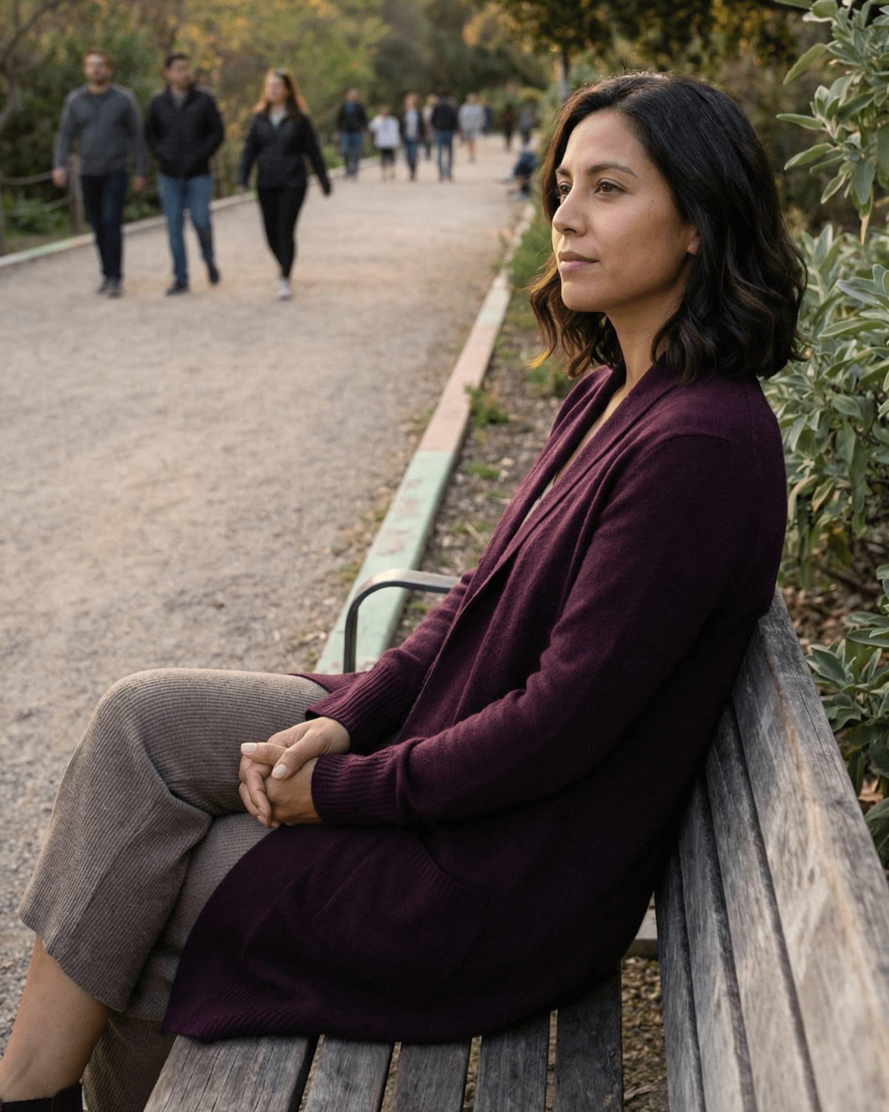 Woman sitting on a park bench, looking away. Wearing a purple sweater and patterned pants, in an outdoor setting.
