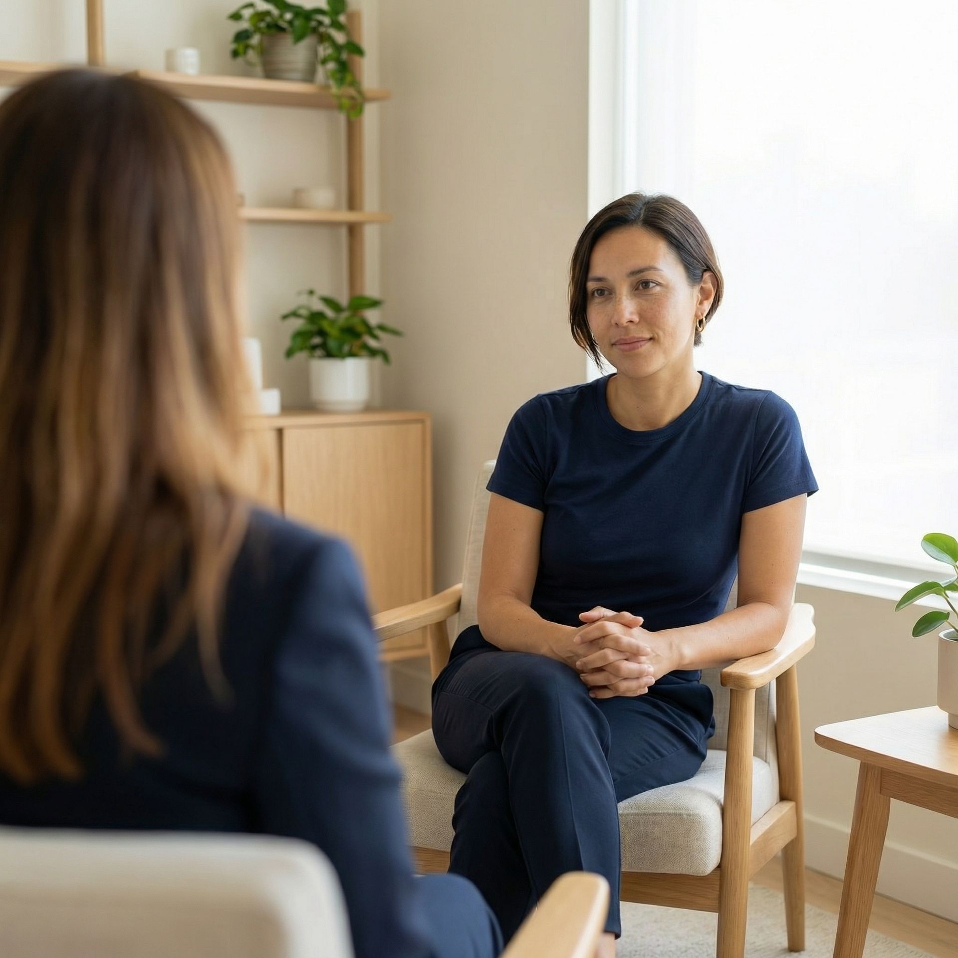Woman in therapy session, sitting and talking with therapist in a well-lit room.