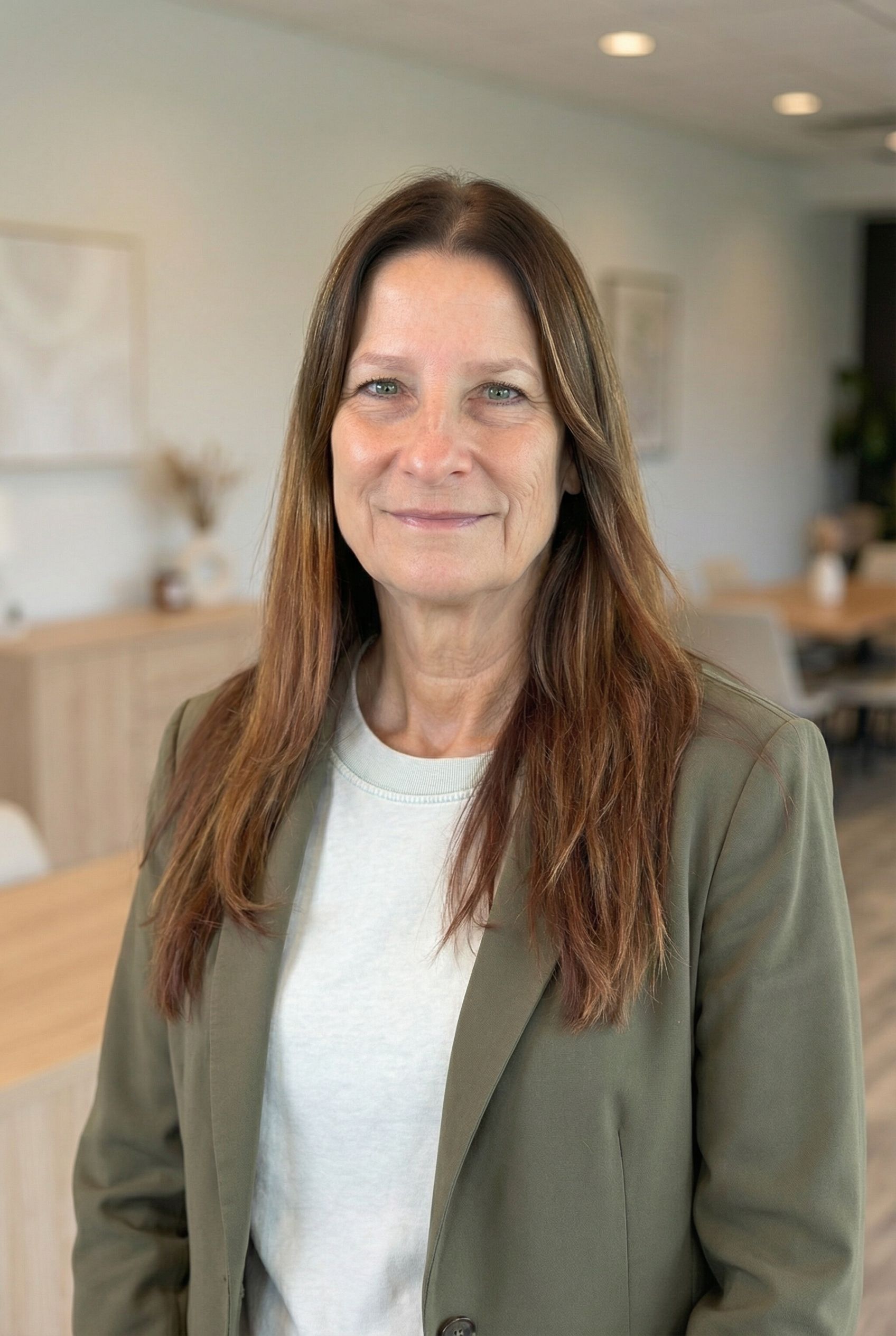 Woman in green blazer smiles at the camera in a modern office.