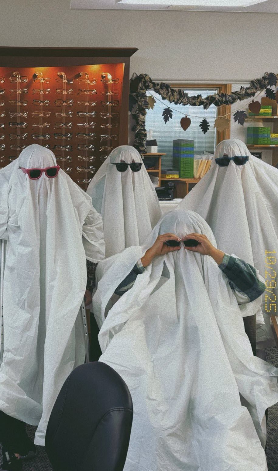 Four people in ghost costumes wearing sunglasses in an optical store. One adjusts glasses.