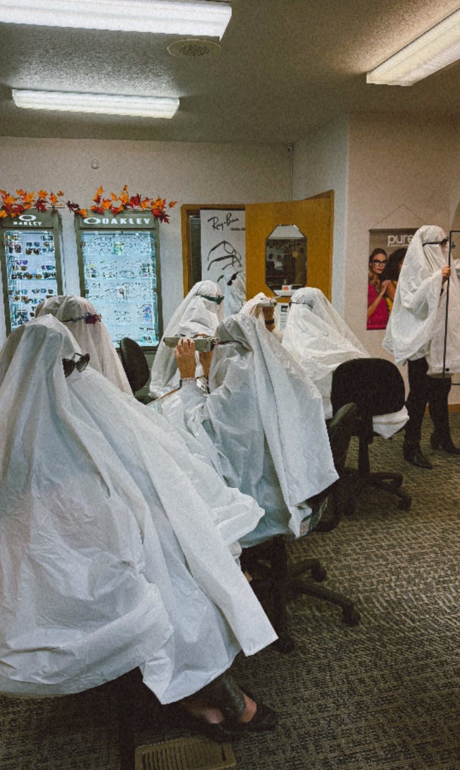 People in white sheets with eye holes sit at desks in an office.
