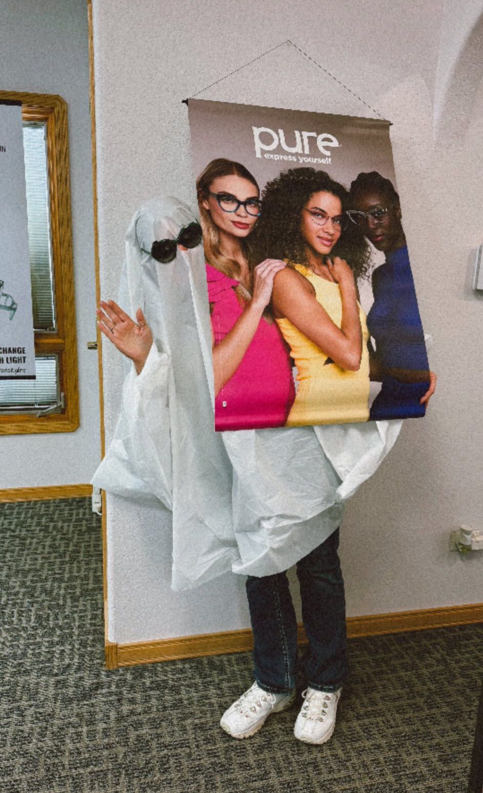 Person dressed as eyeglasses advertisement. Wears white clothes and holds a banner with three people wearing glasses.
