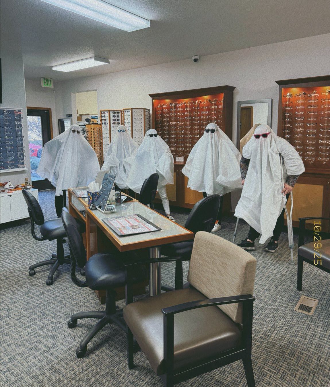 Five people in ghost costumes wearing sunglasses inside an optometry office.