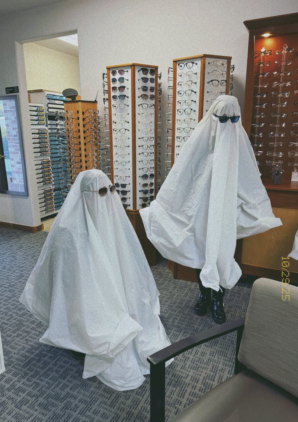 Two figures in white ghost costumes wear sunglasses in an optometry office.