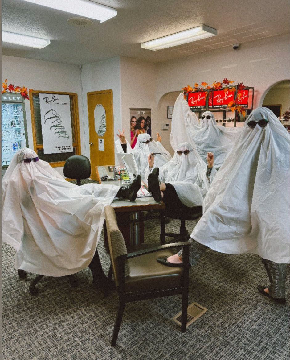 Office workers in white ghost costumes, wearing sunglasses, at desks.