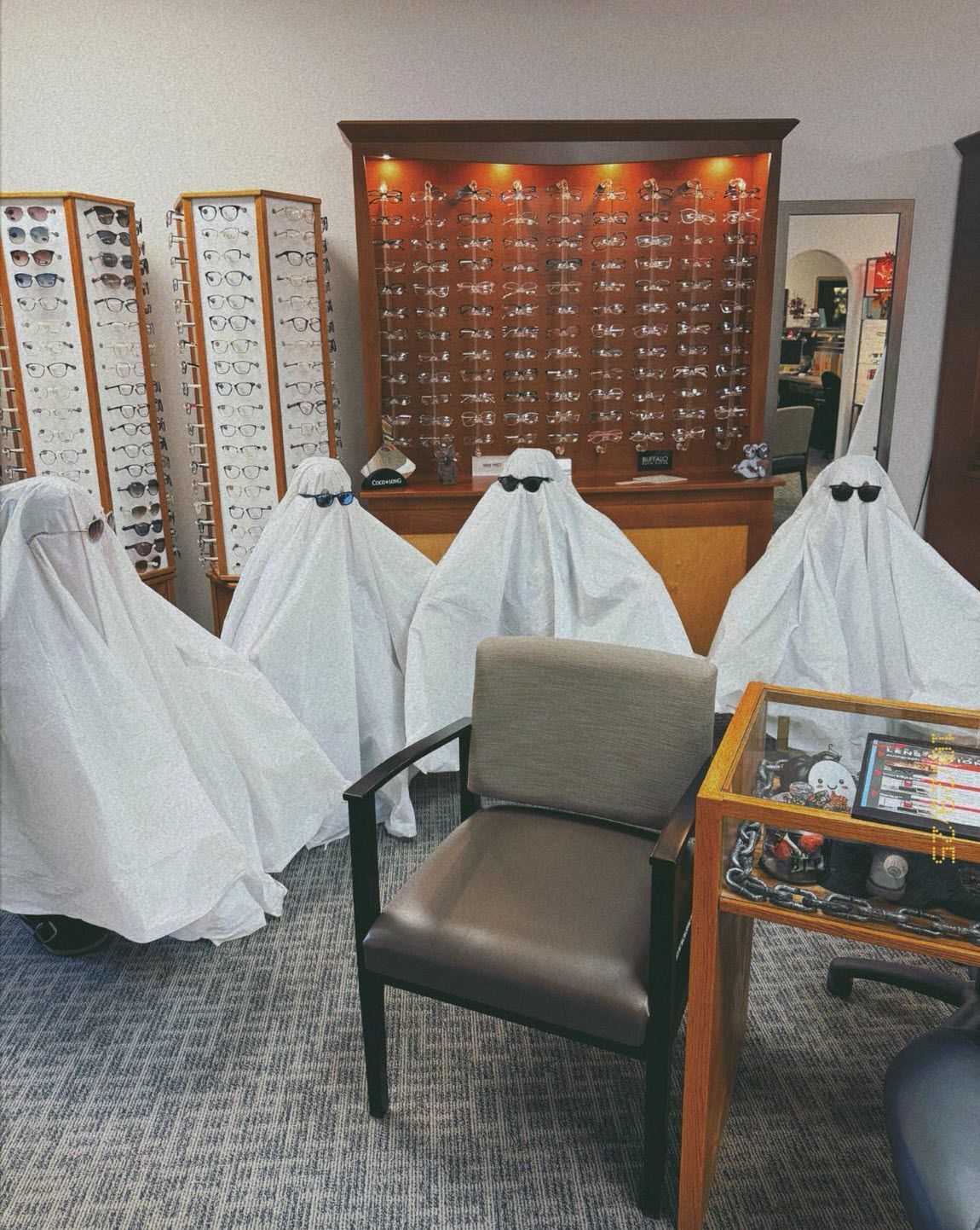 Four ghosts wearing sunglasses in an optical store, looking at eyeglasses.