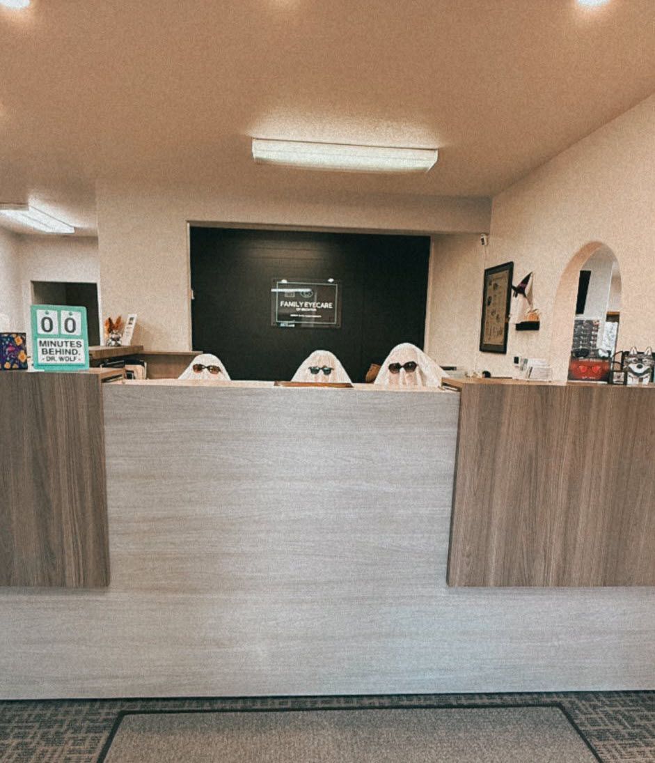 Three people in ghost costumes wearing sunglasses behind a reception desk.