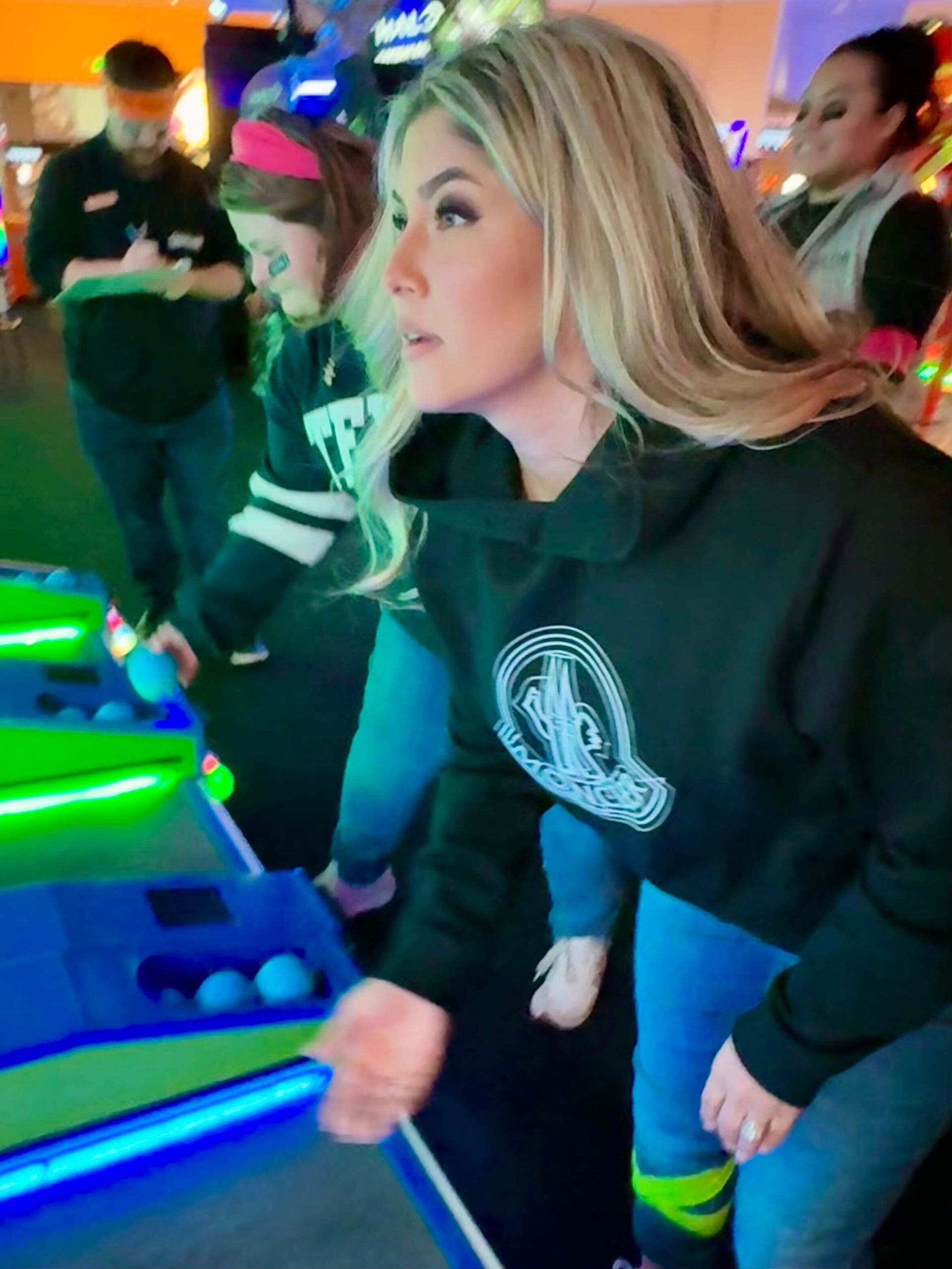 Woman in black hoodie playing arcade game with blue balls, focused expression.