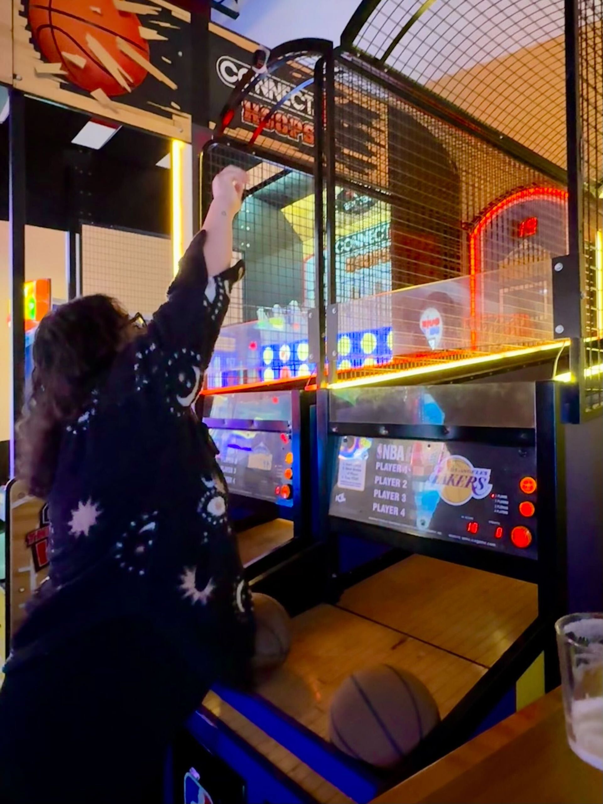 Woman playing basketball arcade game; raising arm to shoot a ball.