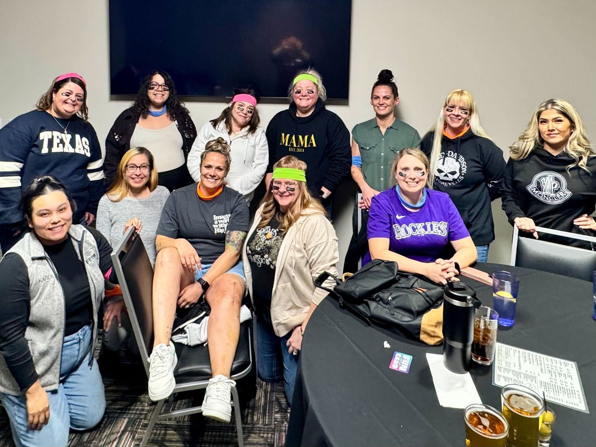 Group of women pose indoors, many wearing neon headbands and themed apparel.