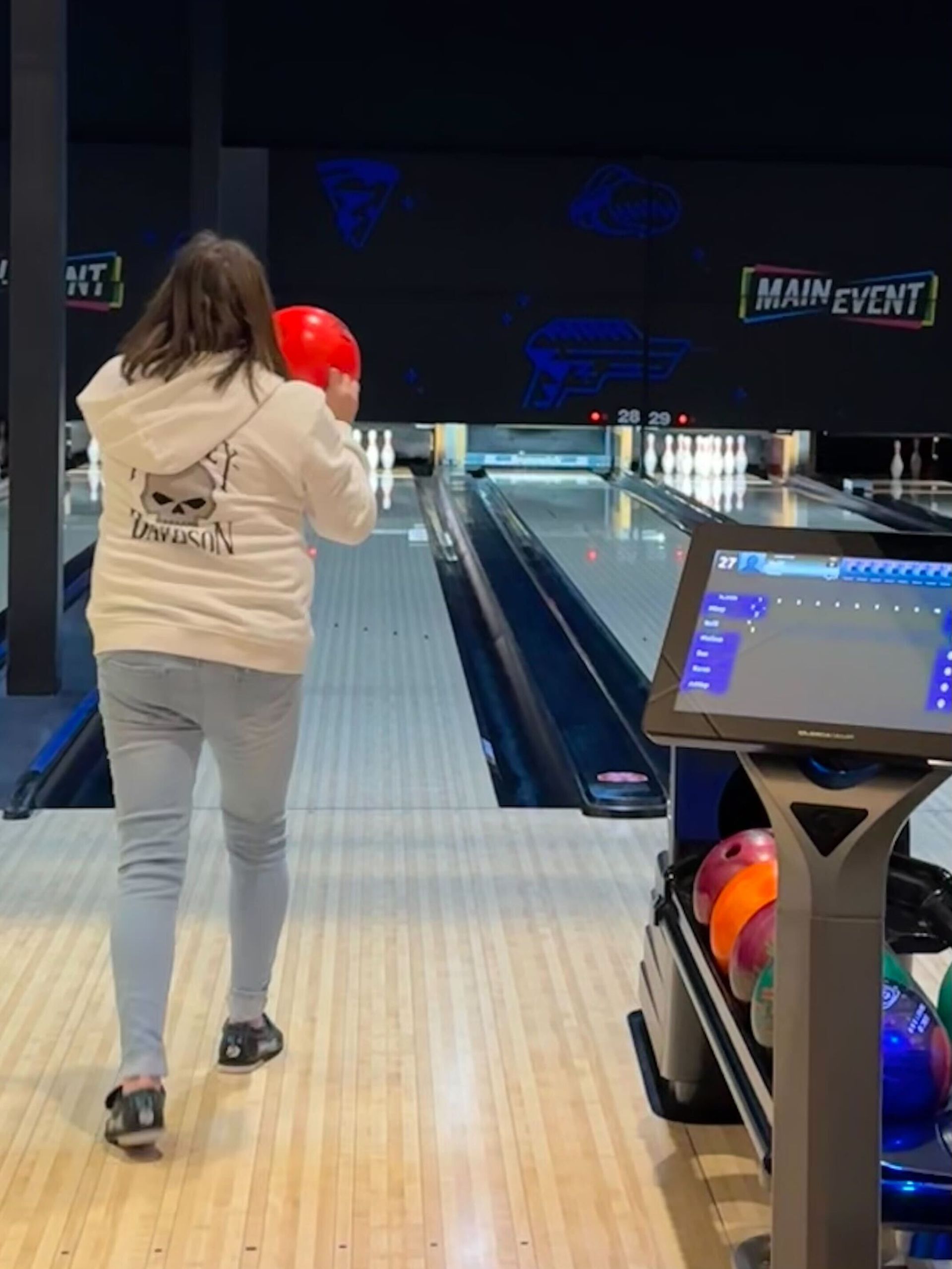 A person bowling at Main Event, holding a red ball.
