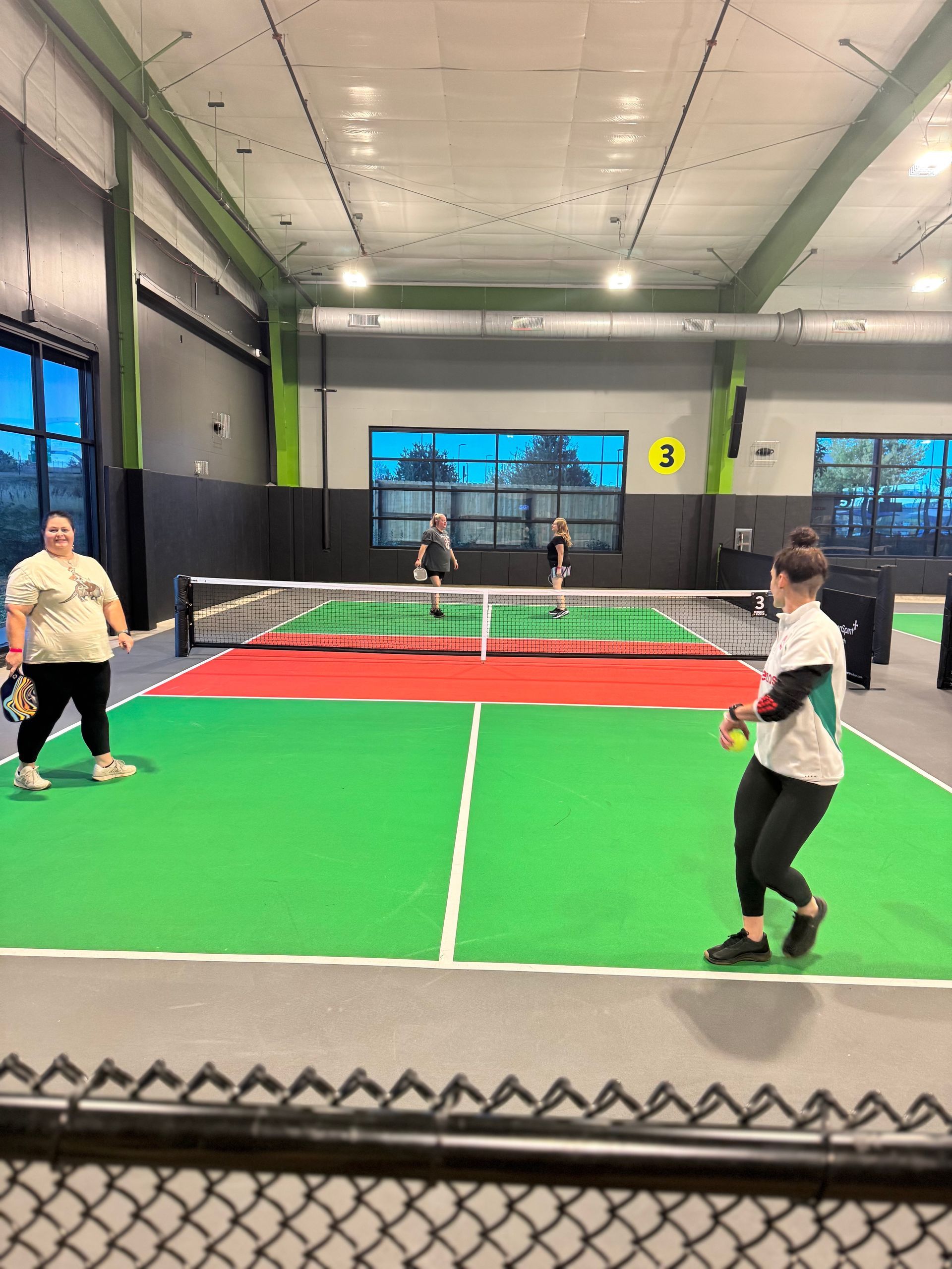 Two teams playing pickleball on a green and red court inside a building.
