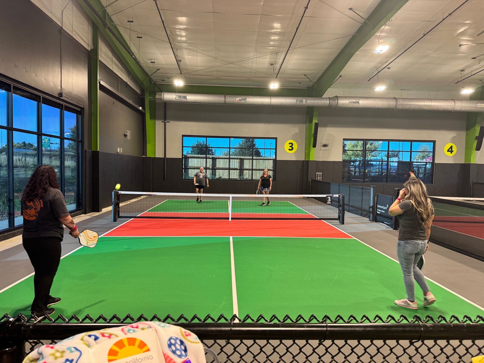 People playing pickleball indoors on a green and red court.