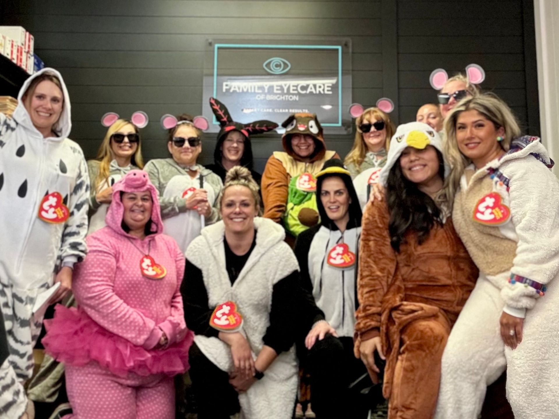 Group of people in animal onesie costumes, smiling in front of a sign for a business.