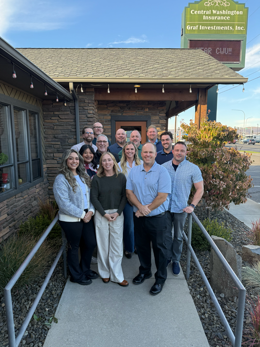 Central Washington Insurance Agency team smiling outdoors in front of wooden sign.