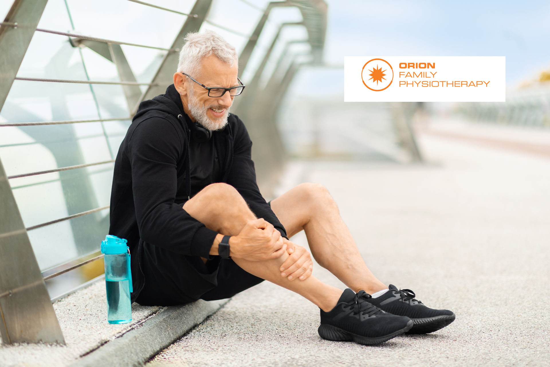 A man is sitting on the sidewalk with his legs crossed and holding his knee.