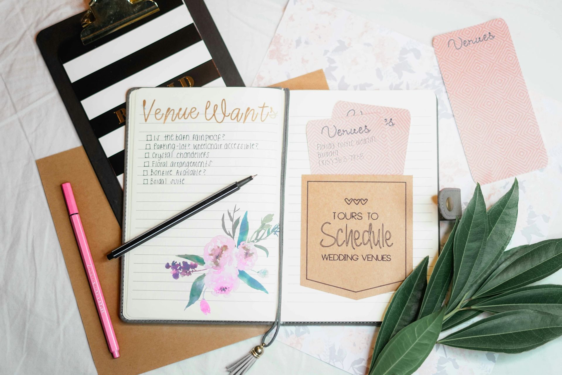 Open planner with floral design, notes, pens, and a clipboard on a table.