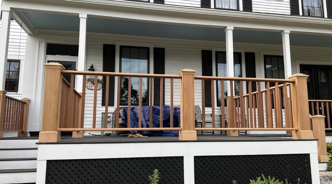A newly constructed light-wood deck railing with thick posts and vertical balusters in front of a white house.