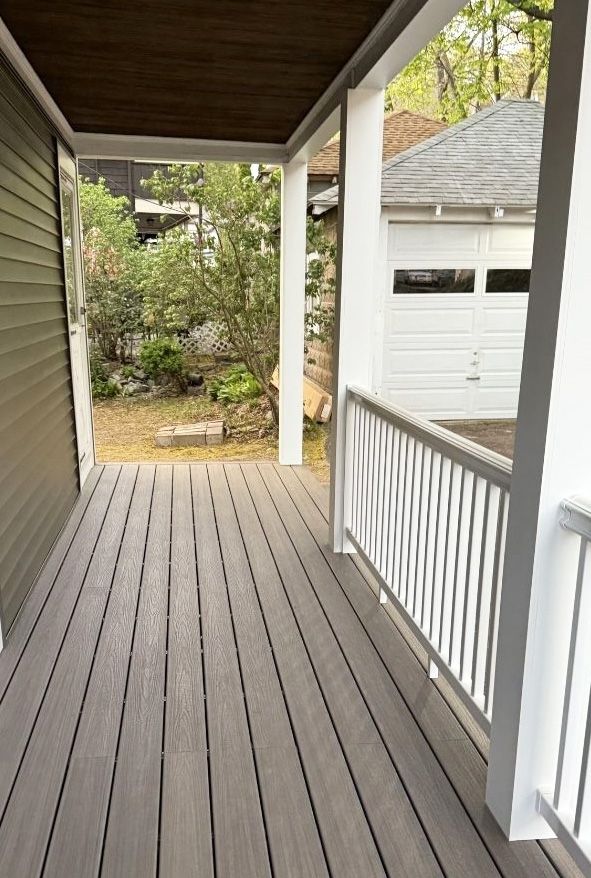 A view from a covered porch with gray composite decking, white railings, and a wooden ceiling, overlooking a backyard.